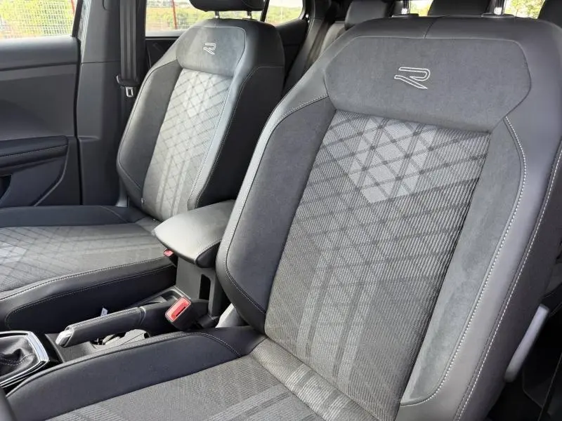 Vue rapprochée des sièges avant gris R-Line avec surpiqûres blanches et logo brodé dans un Volkswagen T-Cross noir nacré.