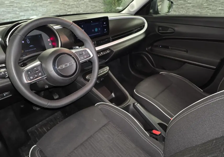 Vue intérieure côté conducteur de la Fiat 600 2024, volant avec logo 600 et tableau de bord numérique moderne.