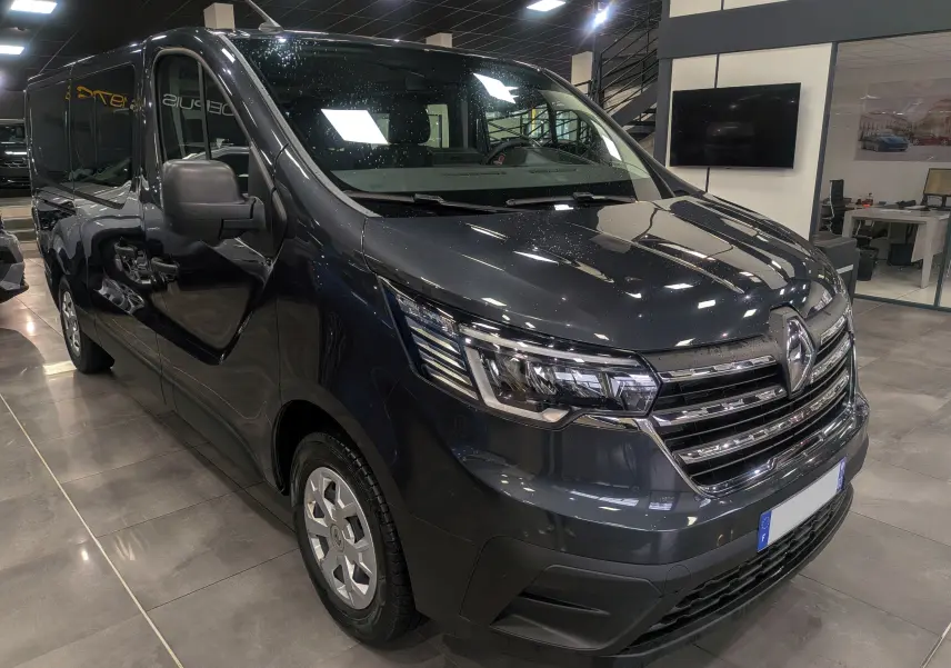 Vue 3/4 avant gauche du Renault Trafic Combi gris Comète 2023, avec calandre chromée et phares LED distinctifs.