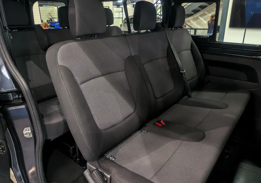 Vue intérieure du siège arrière en tissu gris foncé du Renault Trafic Combi L2 9 places, avec porte coulissante ouverte côté droit.