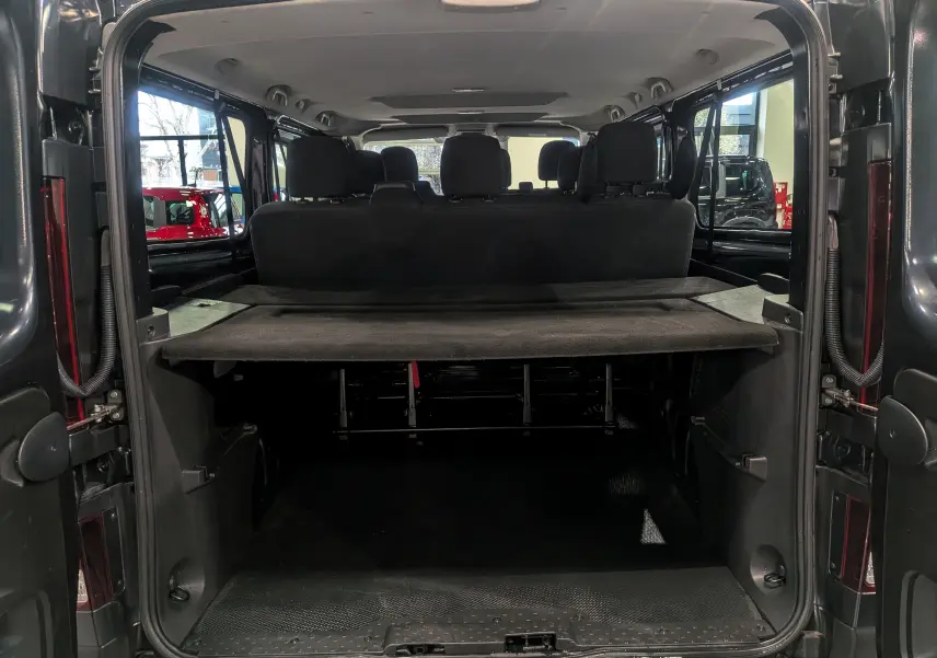 Vue arrière ouverte du Renault Trafic Combi gris Comète 2023, montrant l'espace de chargement et les sièges arrière en tissu noir.
