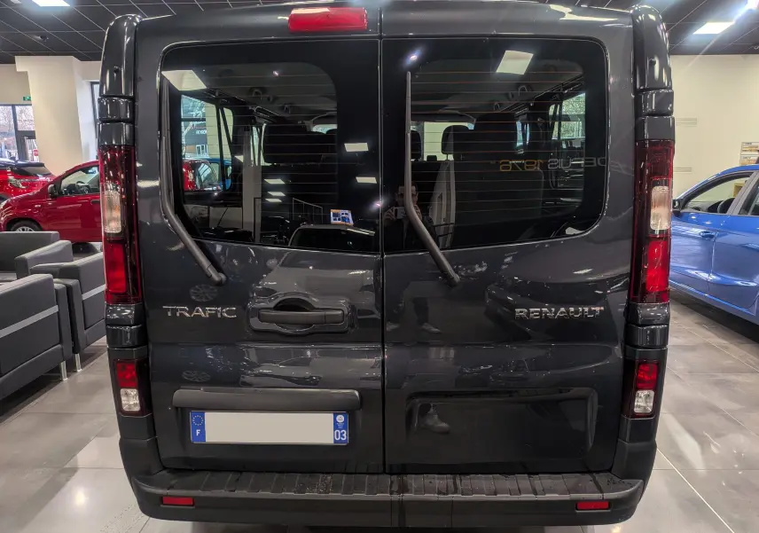 Vue arrière d’un Renault Trafic Combi gris Comète 2023 avec portes battantes et essuie-glaces arrière visibles.