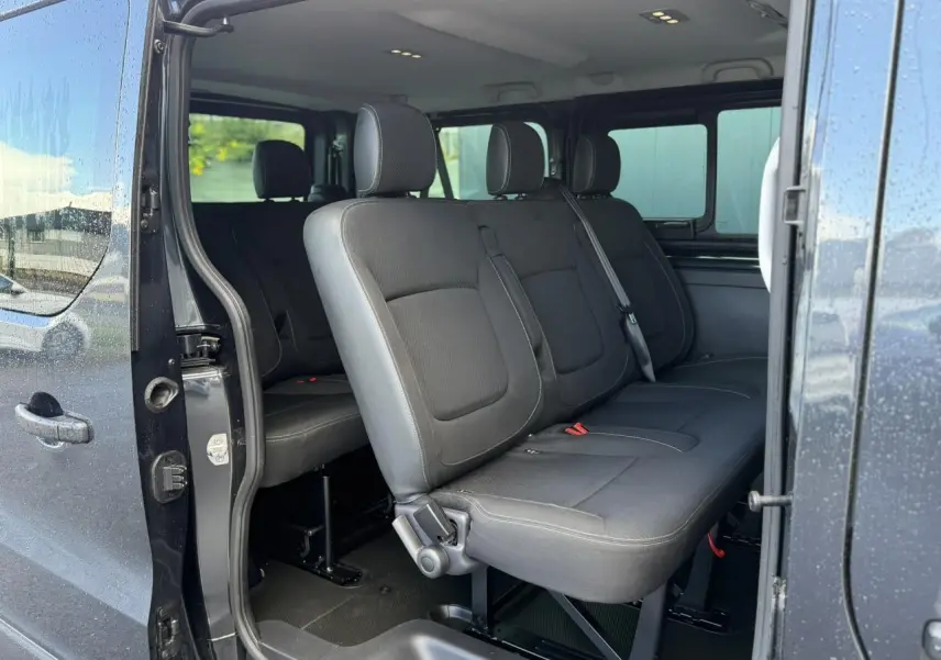 Vue intérieure côté droit du Nissan Primastar Combi gris, montrant les sièges noirs en rangées arrière avec porte coulissante ouverte.