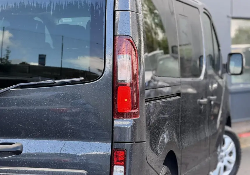 Vue arrière droite du Nissan Primastar Combi gris comète avec hayon vitré et jantes alliage 17 pouces.