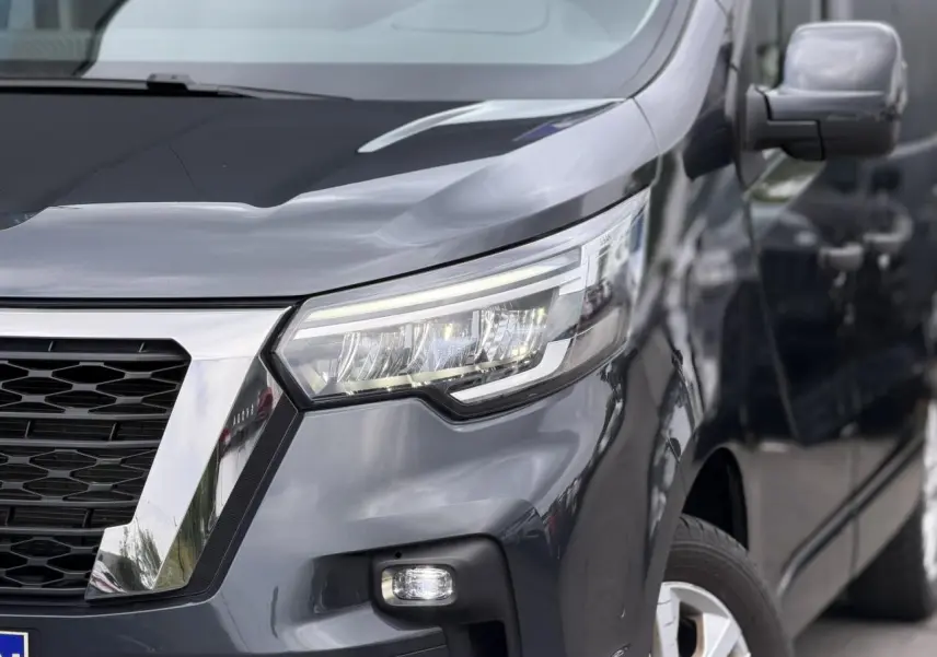 Vue 3/4 avant droit du Nissan Primastar Combi gris Comète, mettant en valeur ses phares LED et la calandre chromée.