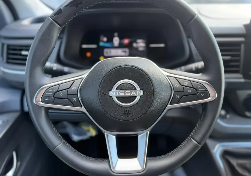Gros plan sur le volant noir du Nissan Primastar Combi 2025 avec commandes intégrées et tableau de bord flou en arrière-plan.
