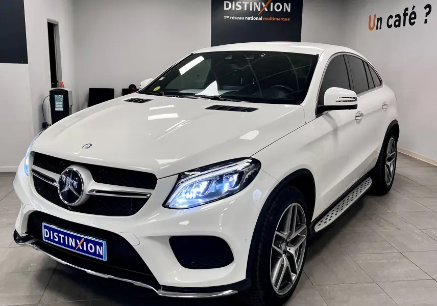 Mercedes GLE Coupe 350 d blanc vue 3/4 avant droit avec phares allumés en intérieur showroom.