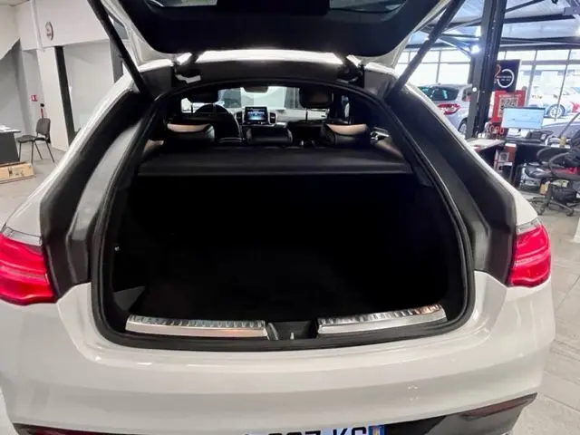 Coffre ouvert en blanc du Mercedes GLE Coupe 350 d 2016 vu de l'arrière dans un garage lumineux.