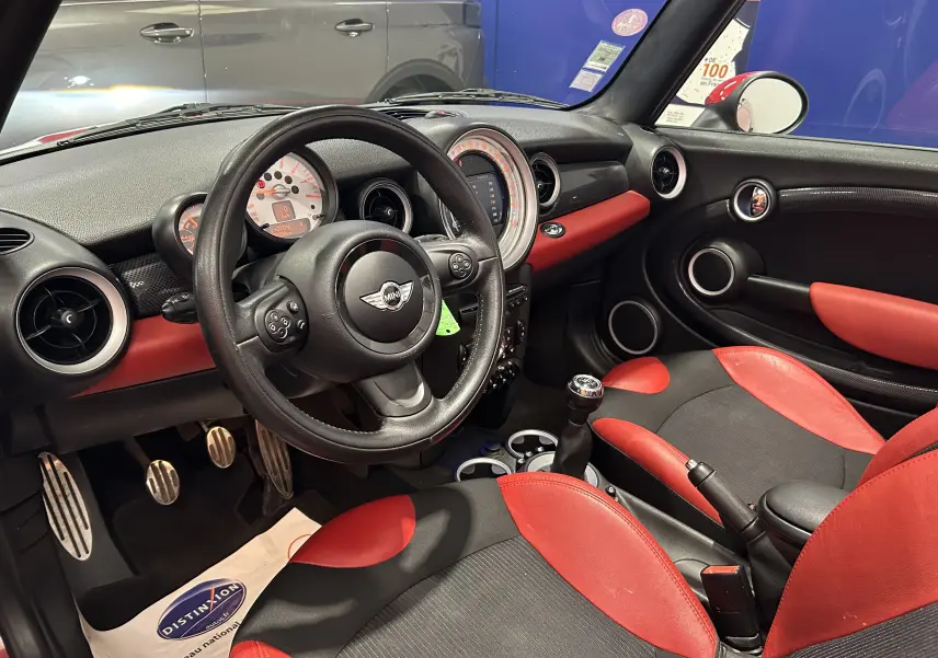 Intérieur avant droit d'une MINI Cabriolet Cooper S rouge de 2012, avec sièges et tableau de bord rouge et noir, volant multifonction.