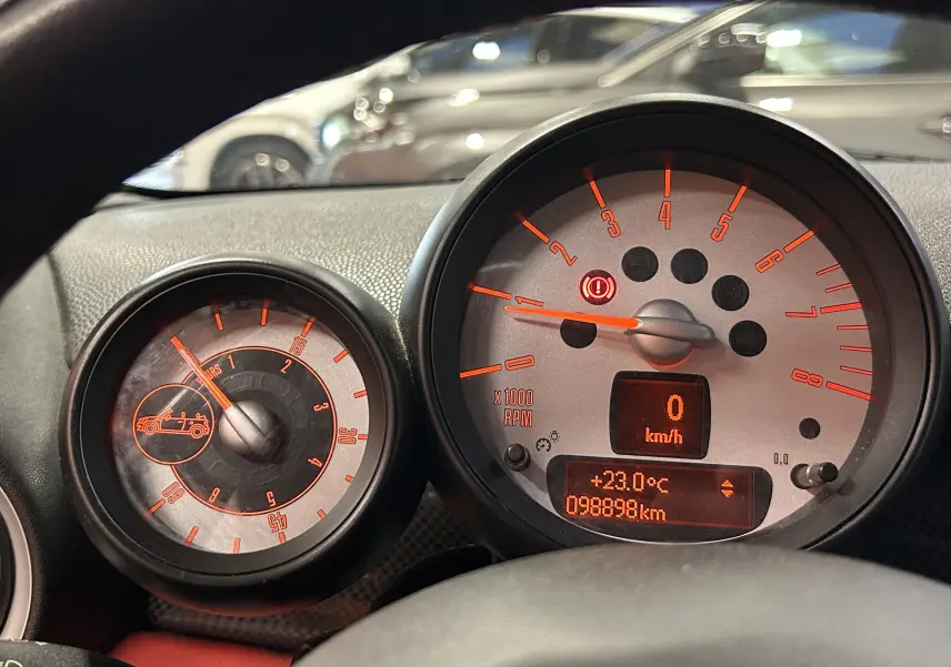 Vue intérieure centrée sur le volant noir de la MINI Cabriolet rouge, avec tableau de bord et commandes lumineuses visibles.