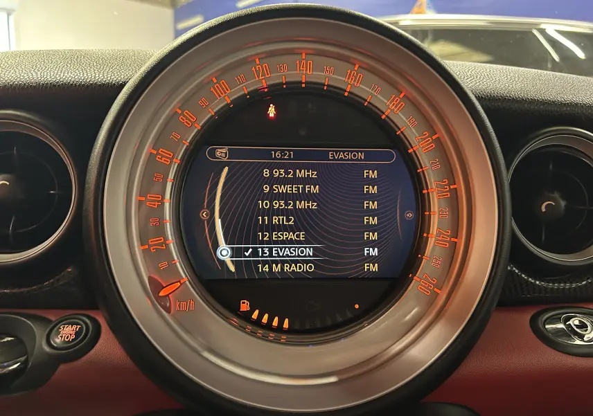 Vue rapprochée du tableau de bord de la MINI Cabriolet rouge 2012, affichant le GPS et le compteur circulaire éclairé en orange.