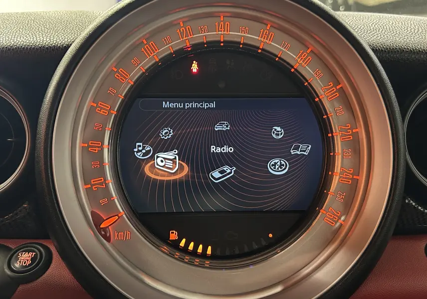 Gros plan sur le tableau de bord circulaire du MINI Cabriolet rouge 2012, affichant le menu principal radio avec éclairage orange.