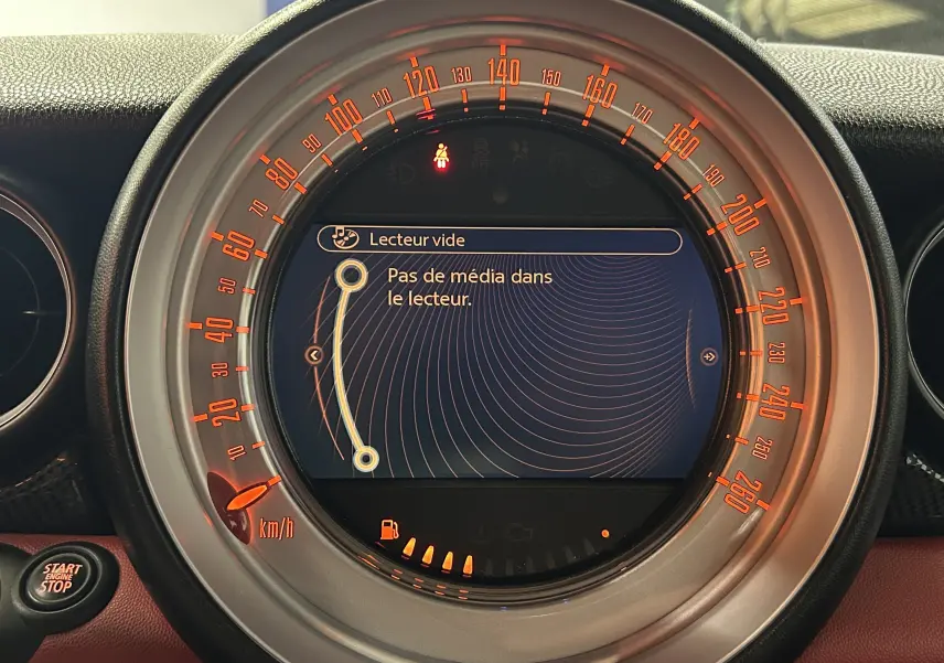 Vue rapprochée du compteur central du MINI Cabriolet rouge 2012, affichant un écran multimédia sans média inséré.