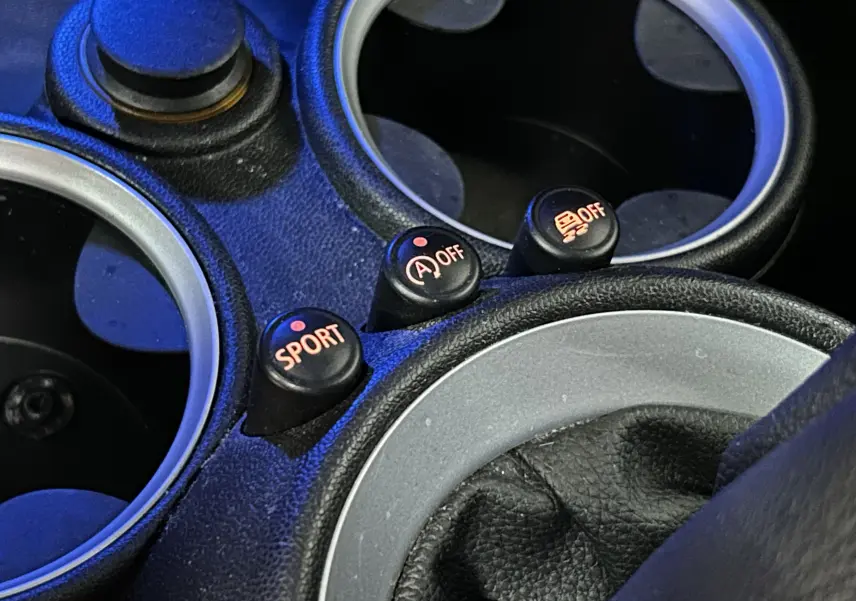 Gros plan sur les boutons SPORT, arrêt auto start et contrôle de traction au centre de la console d'une MINI Cabriolet rouge.