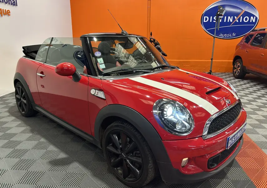 Vue 3/4 avant droite d'une MINI Cabriolet Cooper S rouge avec bandes blanches et jantes noires, capote ouverte.