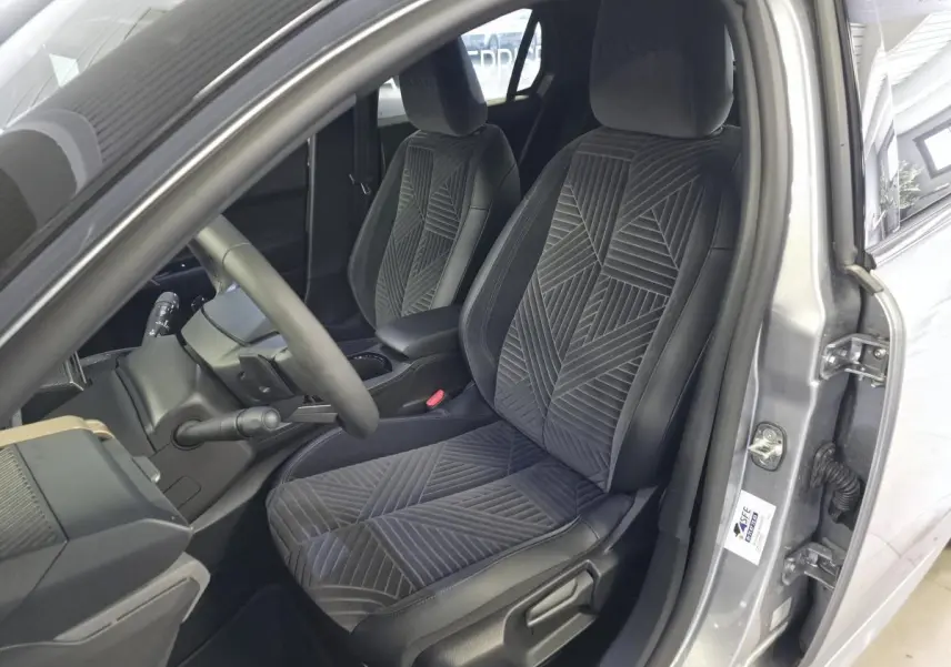 Vue intérieure côté conducteur de la Lancia Ypsilon 2025 gris, avec sièges velours gris à motifs géométriques.