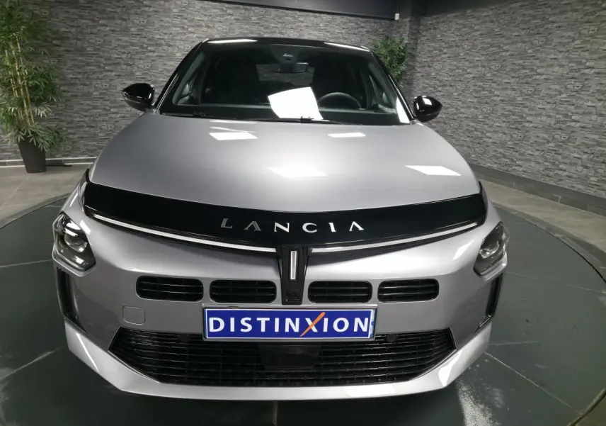 Vue frontale d'une Lancia Ypsilon 2025 gris métallisé avec calandre noire et logo Lancia bien visible.