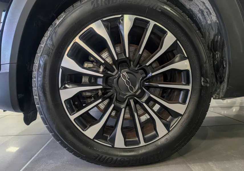 Gros plan sur la roue avant droite du FIAT 500X 2024 noir Cinéma, avec jante alliage bicolore et pneu Bridgestone.