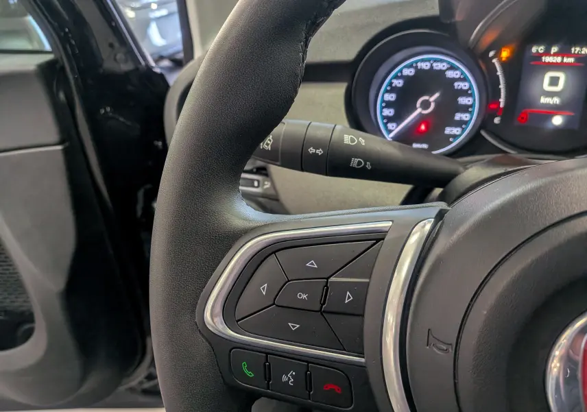 Gros plan sur le volant côté gauche du Fiat 500X 2024 noir, avec commandes intégrées et tableau de bord numérique en arrière-plan.