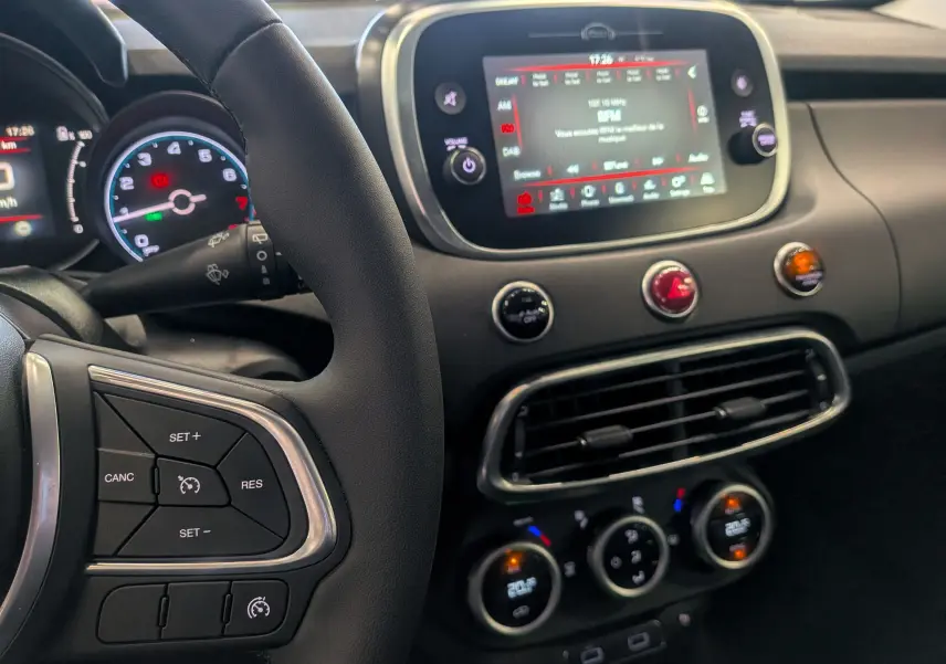 Vue intérieure centrée sur le tableau de bord et le volant noir du Fiat 500X 2024 avec écran tactile et commandes au volant.