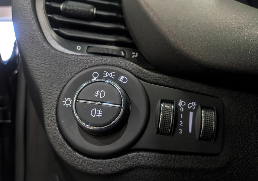 Détail du bouton de commande des feux et réglages d’éclairage sur le tableau de bord noir du Fiat 500X 2024.