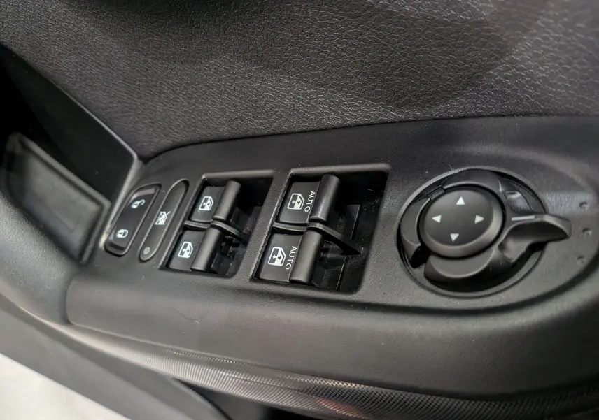 Gros plan sur les commandes de lève-vitres et réglage des rétroviseurs côté conducteur du Fiat 500X noir cinéma 2024.