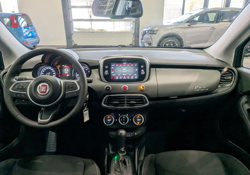 Vue intérieure avant de la Fiat 500X 2024, tableau de bord noir avec écran tactile central et volant multifonction.