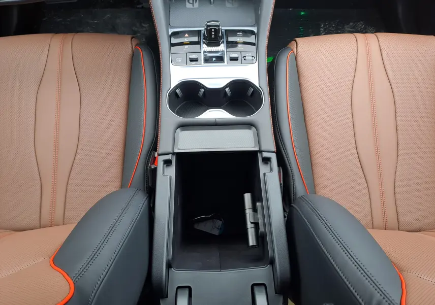 Vue plongeante sur la console centrale ouverte du BYD SEAL U 2025, avec accoudoirs noirs et sièges marron clair à surpiqûres orange.