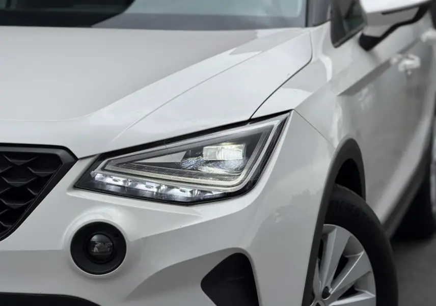 Gros plan sur l'avant droit blanc du SEAT Arona 2025, mettant en valeur le phare LED et le détecteur d'angles morts.