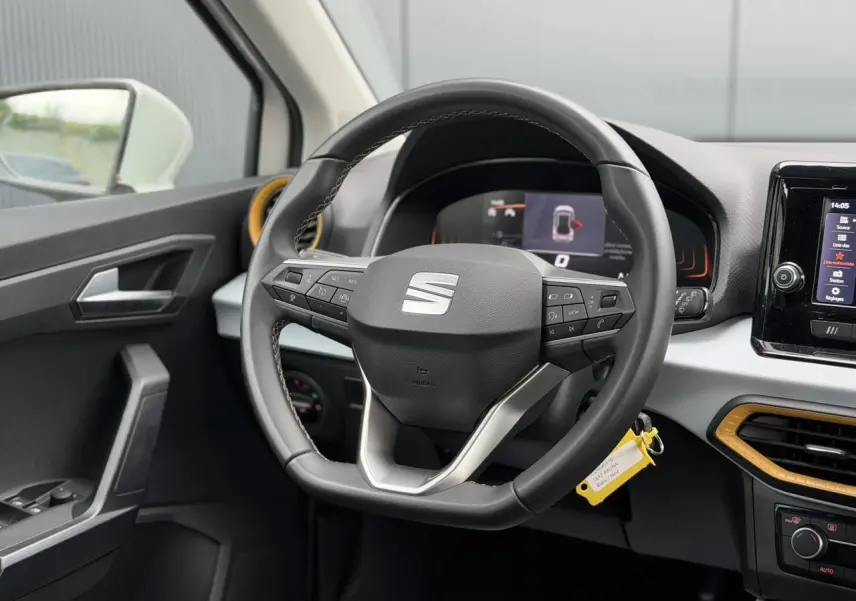 Vue intérieure centrée sur le volant noir du SEAT Arona blanc, avec tableau de bord digital et aérateurs orange.