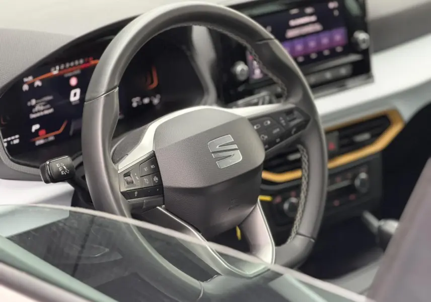 Vue rapprochée du volant noir et du tableau de bord digital du SEAT Arona TSI 115 DSG Style 2025, intérieur moderne.