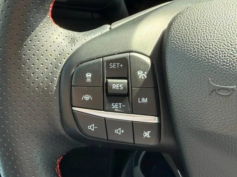 Gros plan sur les commandes multifonctions noires à gauche du volant cuir perforé de la Ford Focus gris lunaire 2025.