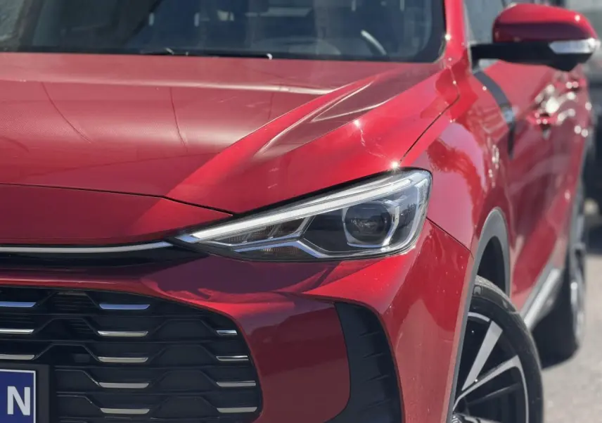 Gros plan sur l'avant droit rouge Diamond du MG ZS 1.5 Hybrid+ 197 Luxury, mettant en valeur le phare LED et la calandre noire.