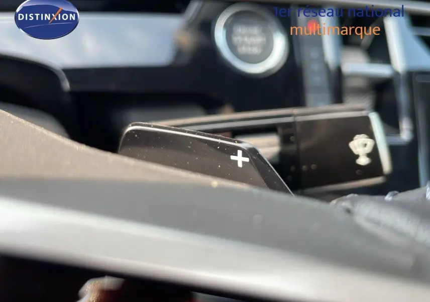Gros plan sur la palette de changement de vitesse "+" du Peugeot 3008 gris, avec bouton start visible en arrière-plan flou.
