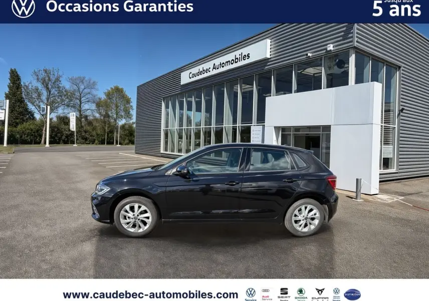 Vue de profil côté gauche d'une Volkswagen Polo 2025 noire intense nacrée, stationnée devant un bâtiment moderne de concession.