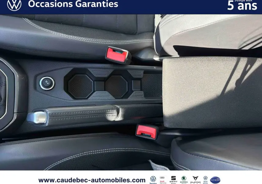 Vue plongeante sur la console centrale et frein à main d’une Volkswagen Polo noire avec sellerie cuir noire et surpiqûres blanches.
