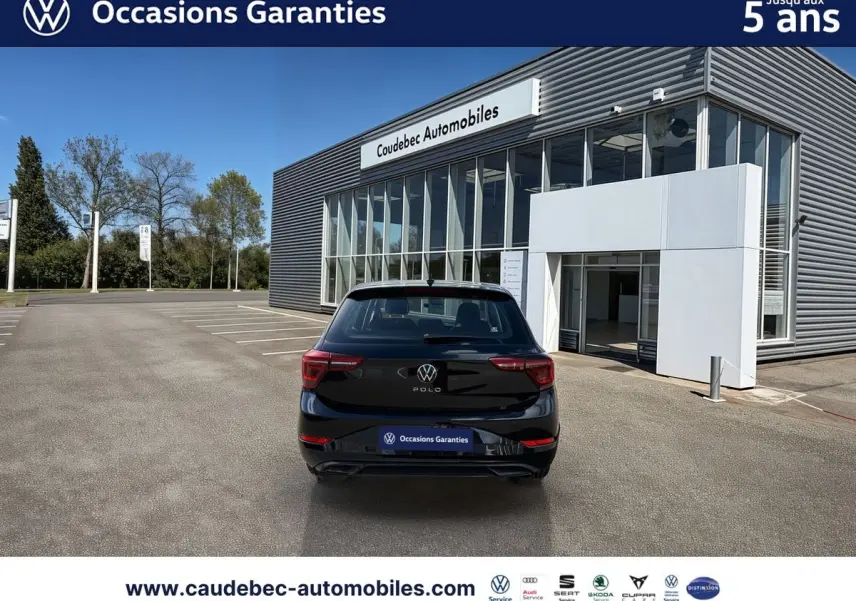 Volkswagen Polo noir intense nacré vue de l'arrière, stationnée devant un bâtiment moderne de concession.