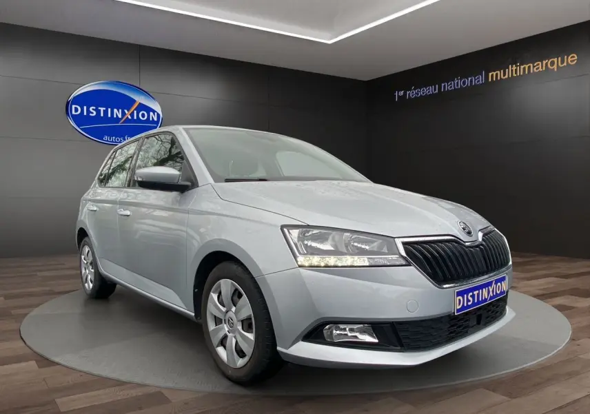 Vue 3/4 avant d’une Skoda Fabia gris argent 2021 avec calandre noire et feux LED allumés en intérieur showroom.