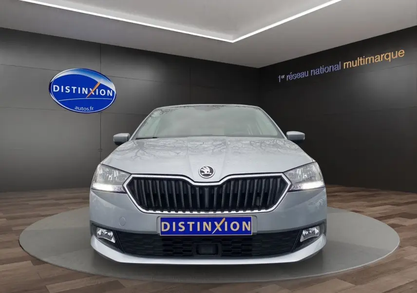 Vue avant d'une Skoda Fabia gris argent 2021 avec calandre noire et phares allumés en showroom.