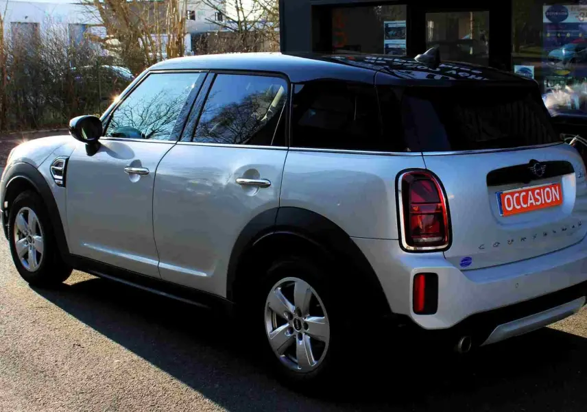 Vue 3/4 arrière droite d'un MINI Countryman gris perle métal avec toit noir, en stationnement devant un bâtiment.