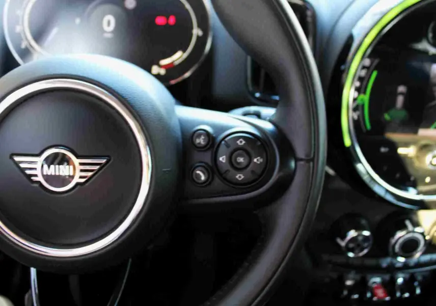Gros plan sur le volant noir de la MINI Countryman II avec commandes intégrées et tableau de bord numérique partiellement visible.