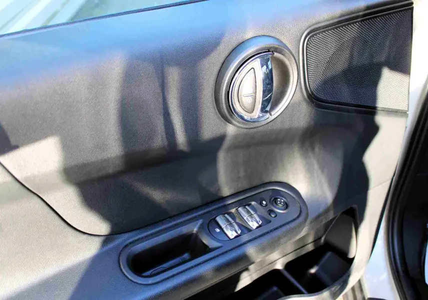 Gros plan sur la porte avant gauche intérieure du MINI Countryman gris perle, avec commandes de vitres et poignée chromée.
