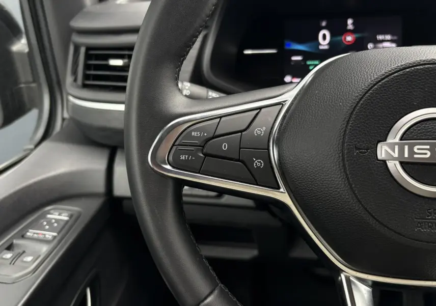 Vue rapprochée du volant noir du Nissan Primastar 2025 avec commandes au volant et tableau de bord numérique flou.