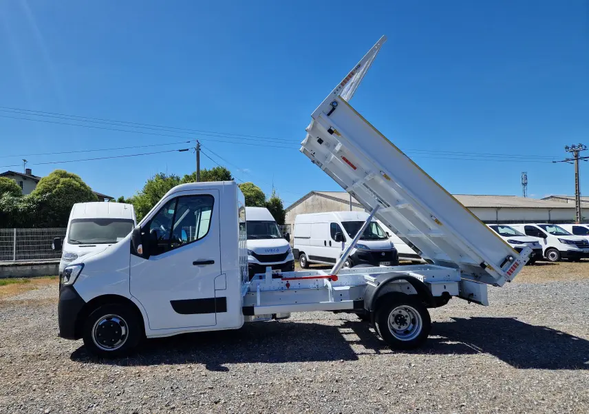 Vue de profil côté gauche du Renault Master blanc avec benne basculante relevée sur un terrain extérieur.