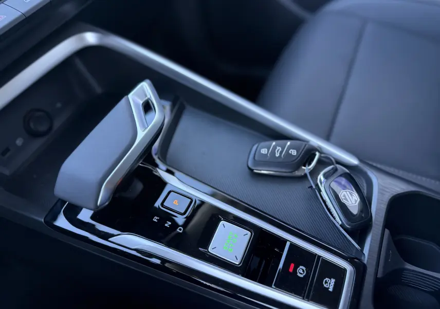 Gros plan sur la console centrale du MG ZS 1.5 L Hybrid+ 197 ch Luxury avec levier de boîte auto et clés sur surface noire texturée.