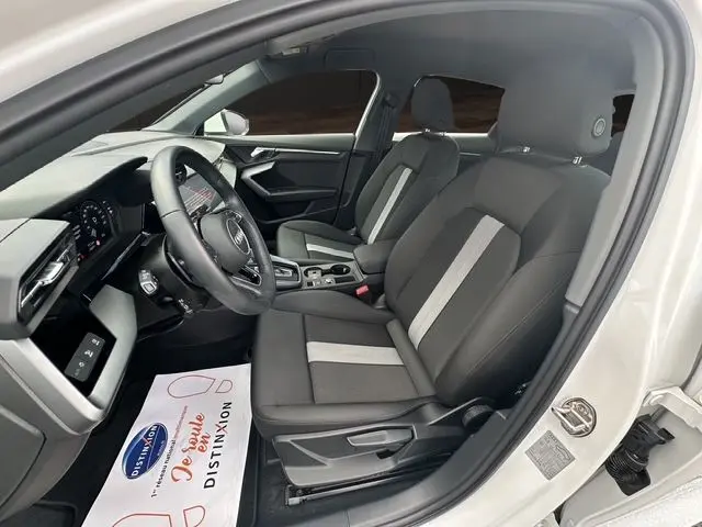 Vue intérieure côté conducteur de l'Audi A3 Sportback 2024 blanc Arkona, sièges tissu noir avec bande grise centrale.