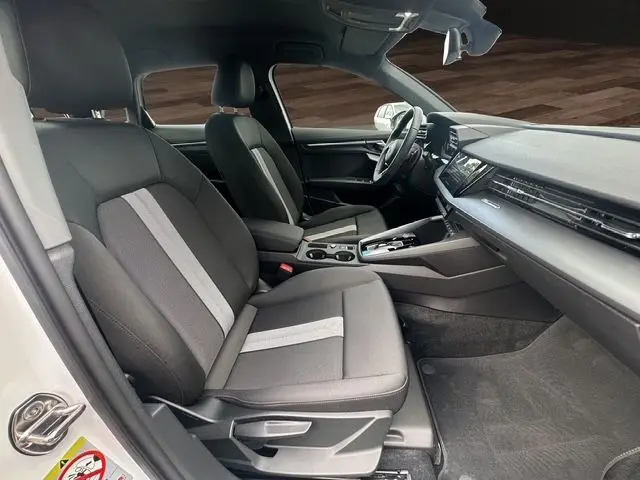 Vue intérieure côté conducteur de l'Audi A3 Sportback 2024 avec sièges tissu noir et bande grise centrale.