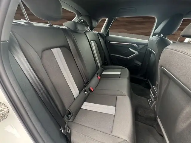 Vue intérieure arrière côté droit de l'Audi A3 Sportback blanc Arkona, sièges tissu noir avec bandes grises centrales.