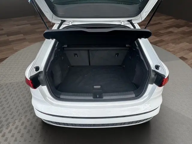 Vue arrière d’un Audi A3 Sportback blanc Arkona 2024 avec coffre ouvert et intérieur de coffre noir visible.