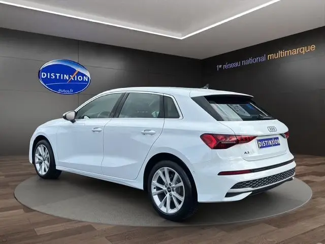 Audi A3 Sportback blanc Arkona vue 3/4 arrière droit en intérieur, avec jantes alliage et feux LED distinctifs.